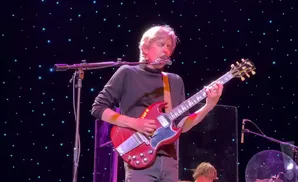 A man plays a red guitar on stage with a starry background.