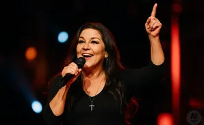 Woman on stage singing into a microphone, pointing her finger up.