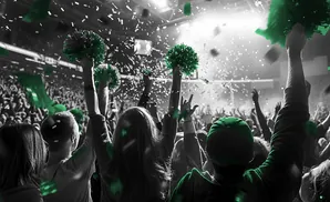 A crowd cheers with green pom-poms and confetti at a concert or sporting event.