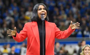 Singer CeCe Winans performs in a red blazer and black turtleneck, with hands extended.