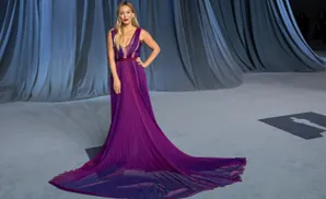 A woman in a flowing purple gown stands with her hand on her hip.