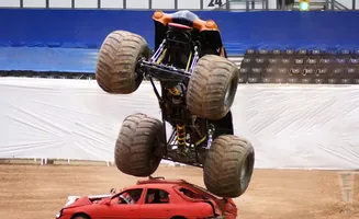 A monster truck crushing a red car in mid-air.