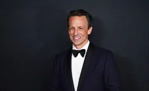 A man in a tuxedo smiles against a dark background.