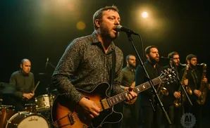 A band performs on stage with a lead singer playing guitar into a microphone.