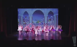 Dancers in tutus perform a ballet on stage with a candy-themed backdrop.