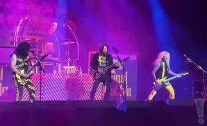 A heavy metal band performs on stage with bright purple and blue lights.