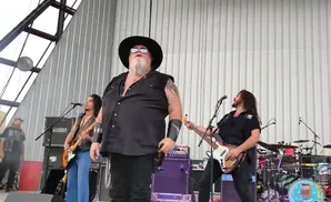 A band performs on an outdoor stage in front of a corrugated metal wall.