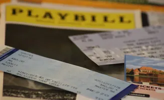 Playbill and tickets, with a postcard of a castle, on a table.