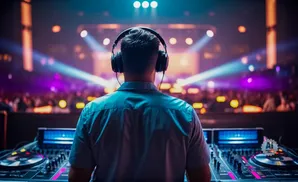 DJ with headphones on, playing music at a club with a crowd and colorful lights.