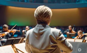 A conductor, viewed from behind, leads an orchestra playing violins.