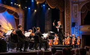 An orchestra performs on stage, conducted by a man in a tuxedo.