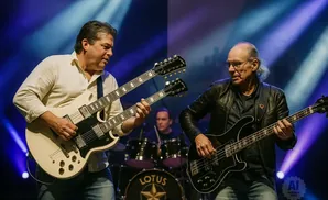 Two men playing guitars on stage with blue lighting.