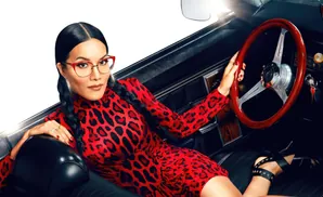 Woman in a red leopard print dress and glasses sits in a car, holding the steering wheel.
