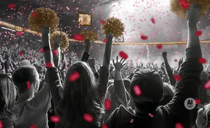 A crowd cheers, holding pom-poms and with red confetti falling.