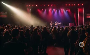 A band performs on a brightly lit stage to an audience at a concert.