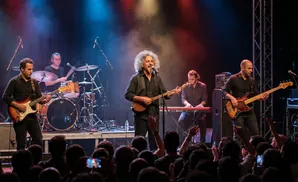 A band performs live on stage with a guitarist, singer, keyboardist, bassist, and drummer.