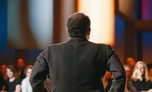 Man in a suit facing away from the camera, speaking to an audience.