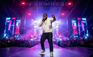 Rapper performs on a brightly lit stage with large screens and an excited crowd.