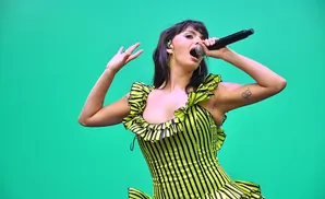 Singer with purple-streaked hair in a neon green and black striped dress sings into a microphone.