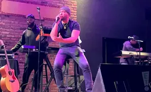 A singer performs on stage with a keyboard player and a guitarist.