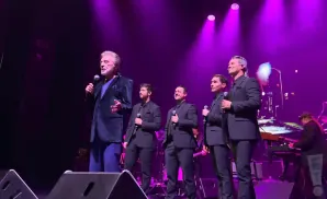 A group of male singers in suits on stage with purple lighting.