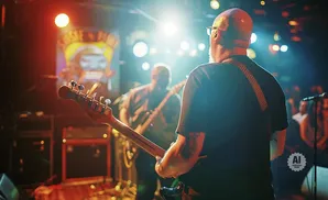 Musicians performing on stage with bright lights and an audience in the background.