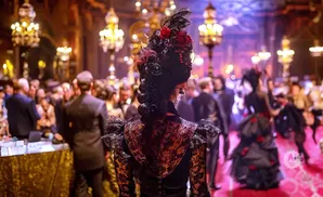 Woman in elaborate gothic dress and hairstyle at a formal masquerade ball.