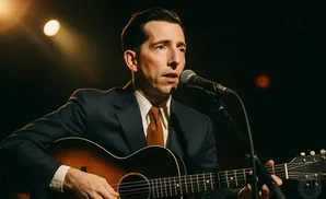 A man in a suit plays an acoustic guitar and sings into a microphone.