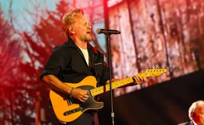Bruce Springsteen sings and plays a yellow guitar on stage with a blurry red backdrop.