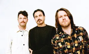 Three men in dark clothing pose against a white background.