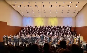 An orchestra and choir perform on a brightly lit stage.