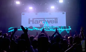 DJ Hardwell performs for a cheering crowd at a concert with his name displayed on a large screen.