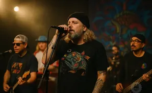 A band performs on stage; the lead singer wears a black beanie and a t-shirt with a fish graphic.