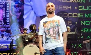 A man in a white t-shirt and bandana performs on stage with a band.