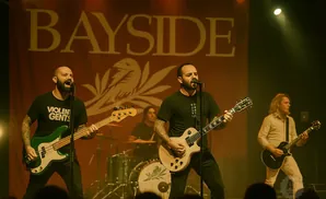 A band performs on stage in front of a large banner with the word 