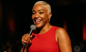 A Black woman with short blonde hair smiles broadly while holding a microphone, wearing a red dress.