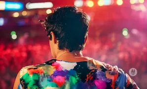 Rear view of a person in a colorful floral shirt on stage with a crowd in the background.