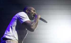 A Black man in a white t-shirt sweats as he raps into a microphone on stage.