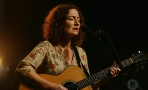 Woman singing and playing guitar with a floral print top.
