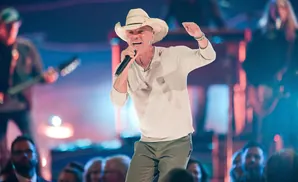 A man in a cowboy hat sings into a microphone on stage.