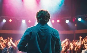 A man stands on a stage with his back to the camera, facing a cheering crowd.