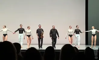 Dancers and musicians on stage, some in leotards and tights, one holding a violin.