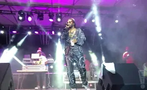 A rapper in a patterned suit performs on a smoky stage under purple lights.