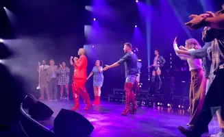 People on a stage in red boots and colorful outfits, some cheering.