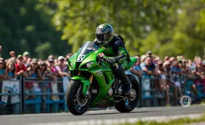 A green motorcycle rider speeds past a blurred crowd at a race.