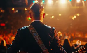 Back of a man in a suit playing guitar on stage with a cheering audience.