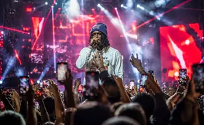 A rapper performs on stage with red lights and a crowd holding up phones.