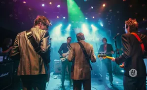 Band on stage playing guitars with stage lights and fog.