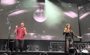 Shania Twain and an unidentified man perform on stage, with a disco ball above them and screens displaying a starry background.