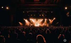 A band performs on a brightly lit stage to a large, dark crowd at a concert.